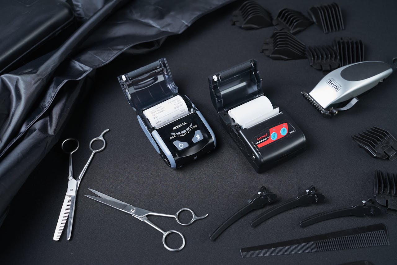 Top view of professional hairdressing tools including scissors, clippers, and combs on a dark surface.
